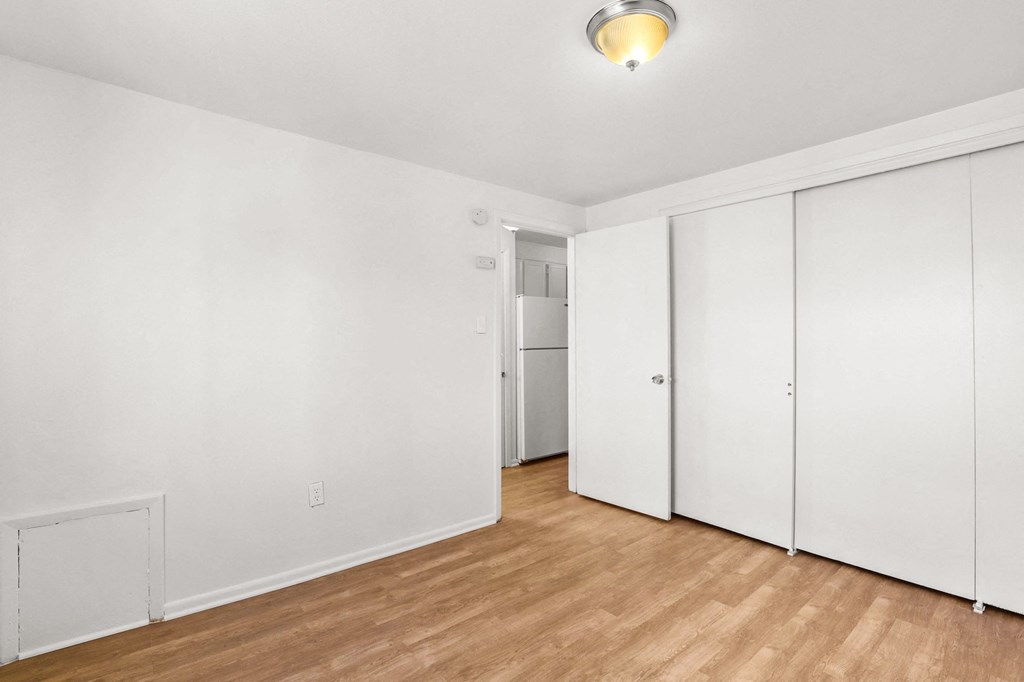 a bedroom with white walls and wood floors and a closet