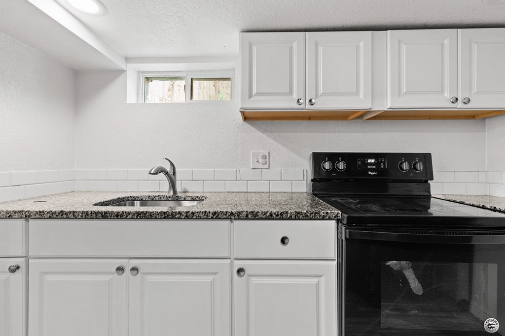 a kitchen with white cabinets and a black stove and sink