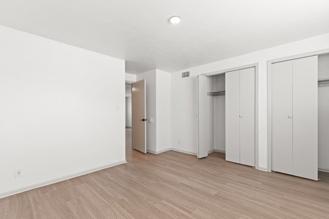 a bedroom with white walls and wood flooring and white closets