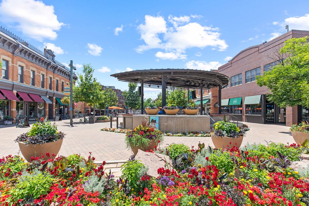 A sunny day in a town square with a gazebo and flower beds.