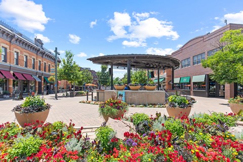 A sunny day in a town square with a gazebo and flower beds.