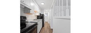 A long hallway with white walls and a black refrigerator.