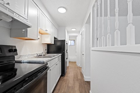 A long hallway with white walls and a black refrigerator.