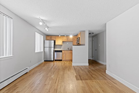 an empty living room and kitchen with wood flooring and white walls
