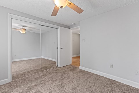 an empty bedroom with a ceiling fan and mirrored closet