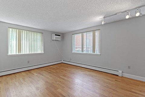 the living room of an empty house with wood flooring and two windows
