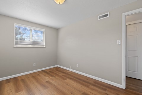 A room with a wooden floor and a window with blinds.