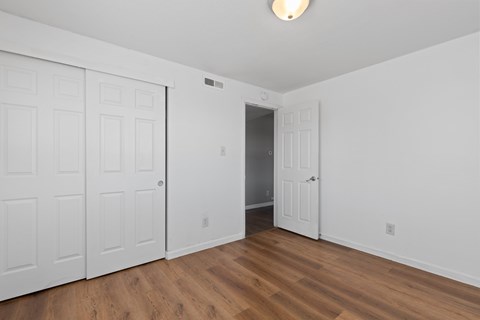 A room with white walls and wooden floors, with a door on the right side.