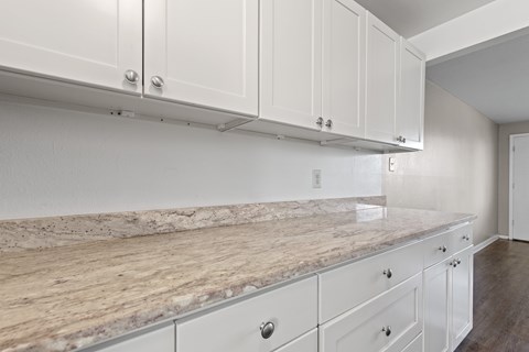 A kitchen with white cabinets and a marble countertop.