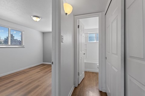 A hallway with white walls and wood floors leading to a door.