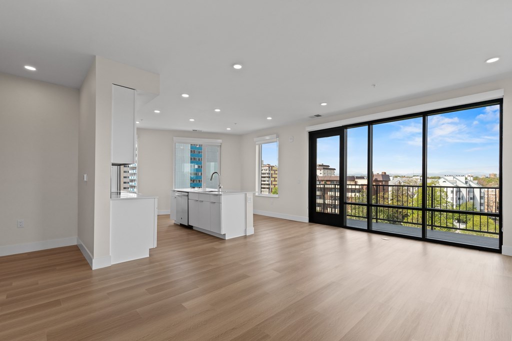 A large empty room with wooden floors and a view of the outside through the sliding glass doors.
