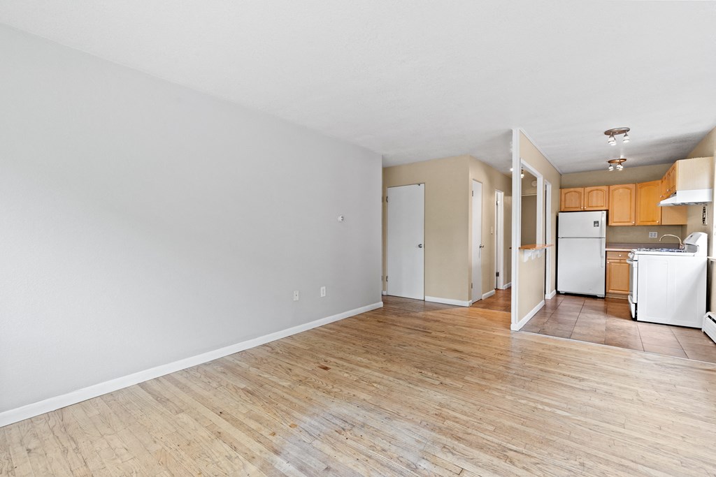 an empty living room and kitchen with wood flooring and white appliances