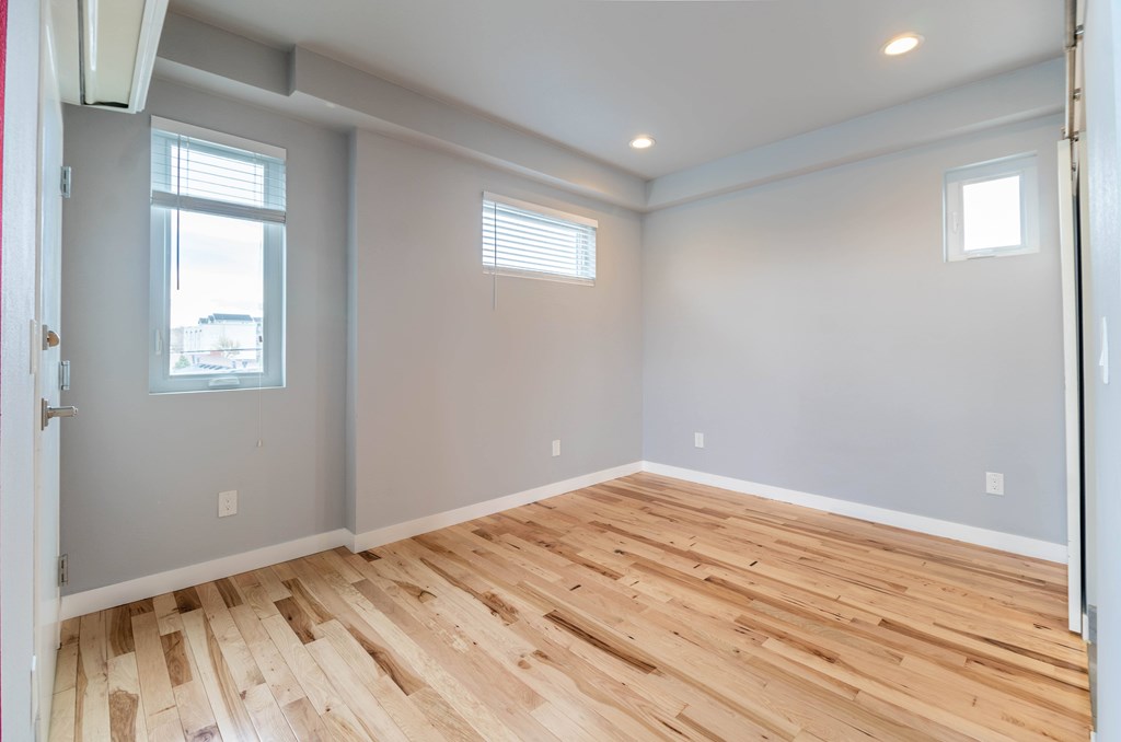 A room with wooden flooring and two windows.