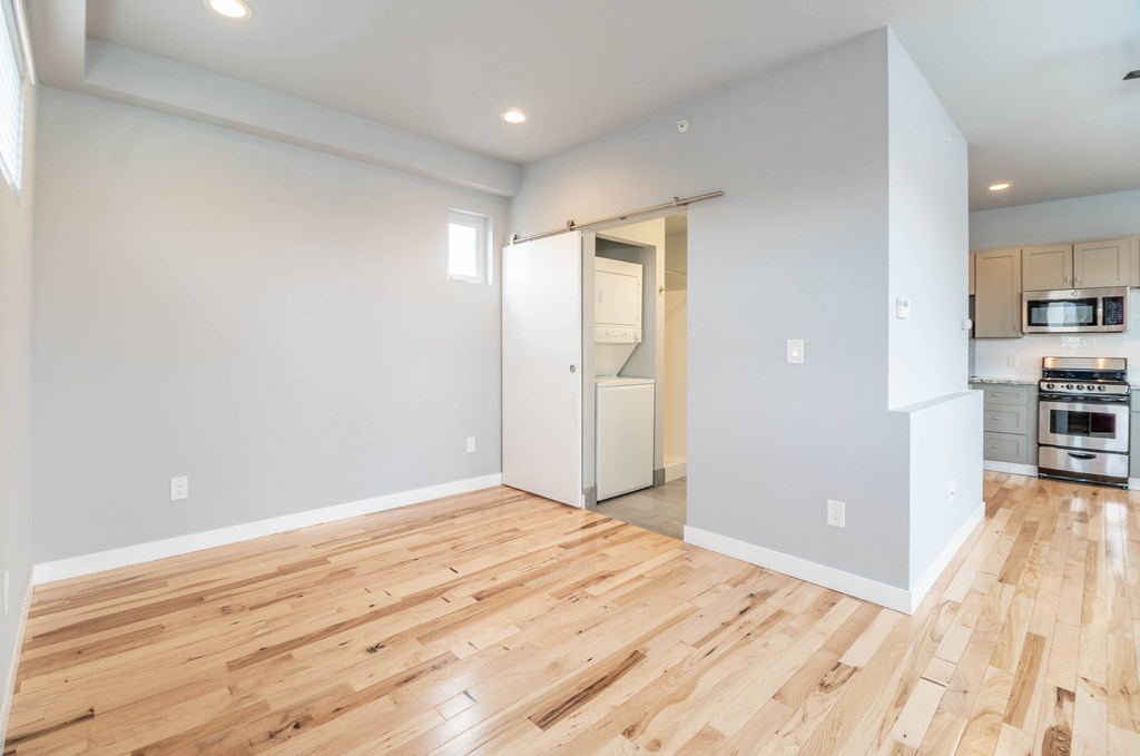 A room with wooden flooring and a kitchen area in the background.