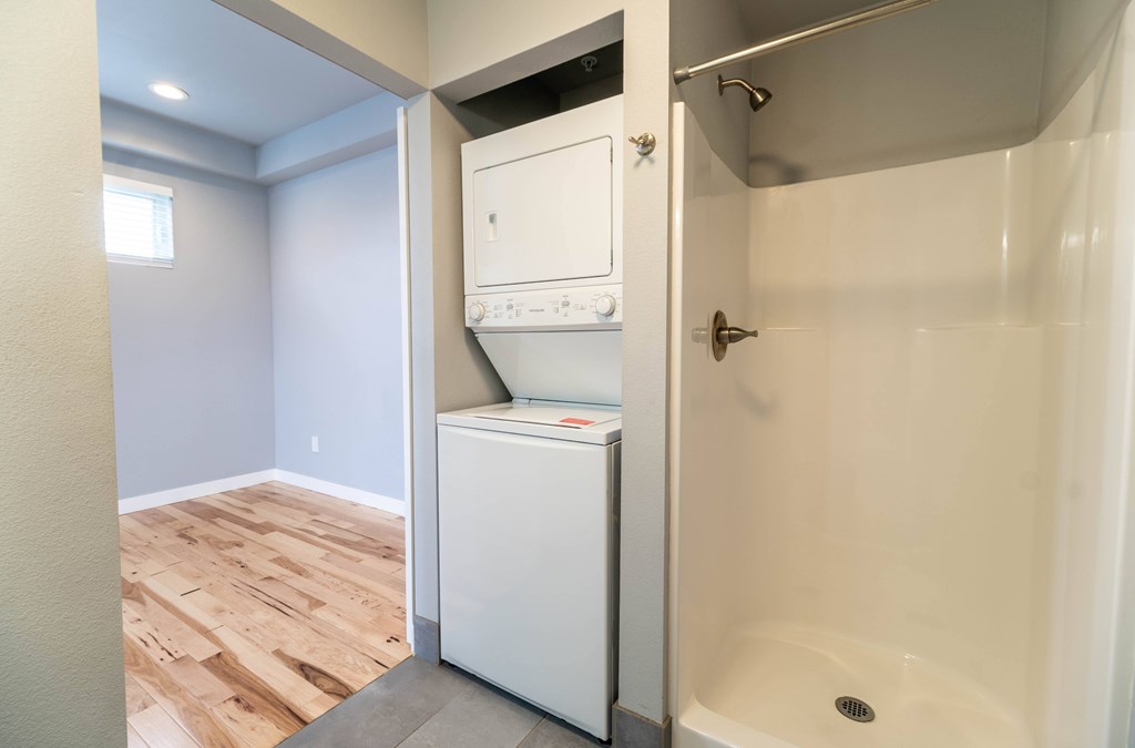 A white dishwasher is in a small bathroom with a walk-in shower.