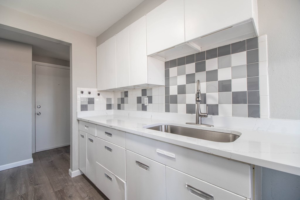 A kitchen with white cabinets and a checkered backsplash.