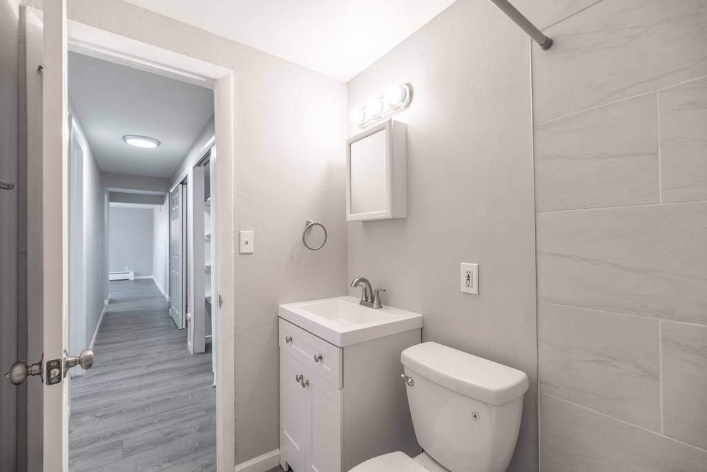 A white bathroom with a toilet, sink, and a mirror.