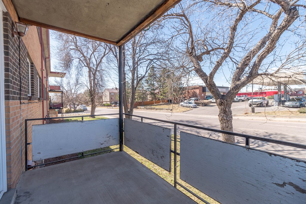 A concrete balcony with a metal railing and a tree in the background.
