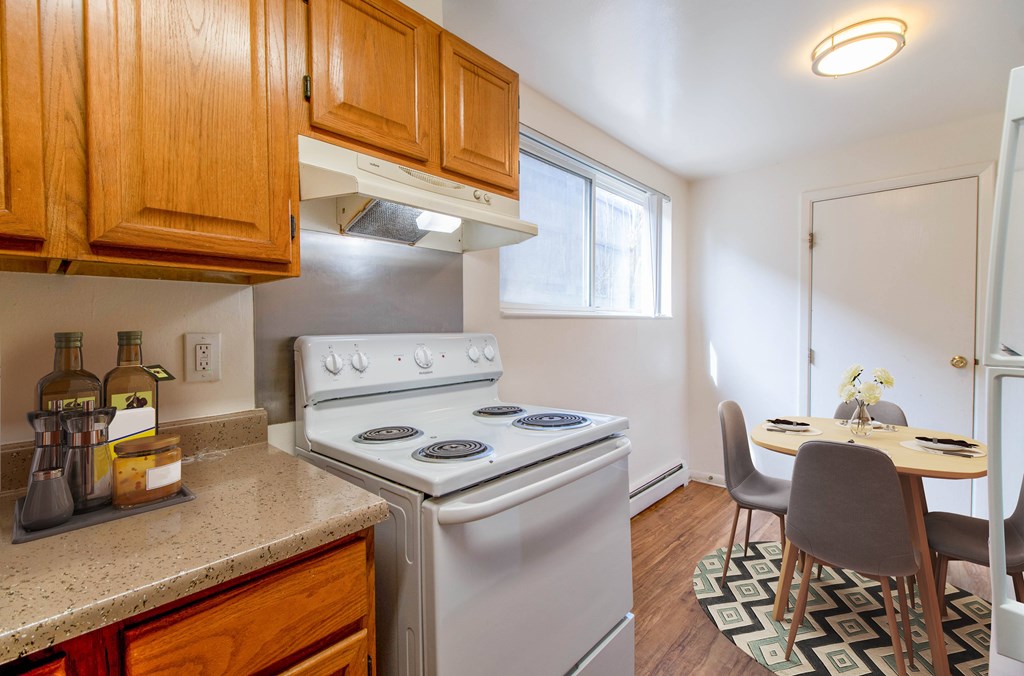 A kitchen with a stove top oven and a dining table with chairs.