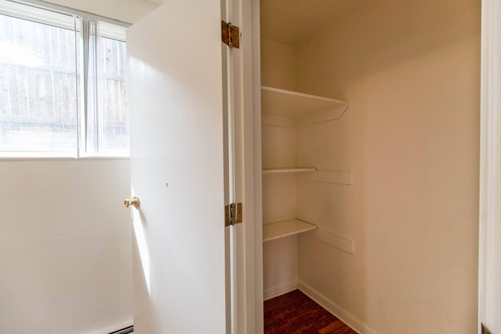 A white door with a gold handle is open to a room with a white wall and a wooden floor.