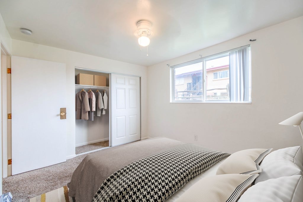 A bedroom with a bed, a window, and a closet with clothes hanging.