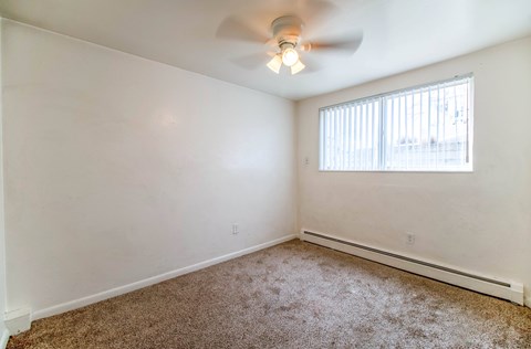 A room with a ceiling fan and a window with blinds.