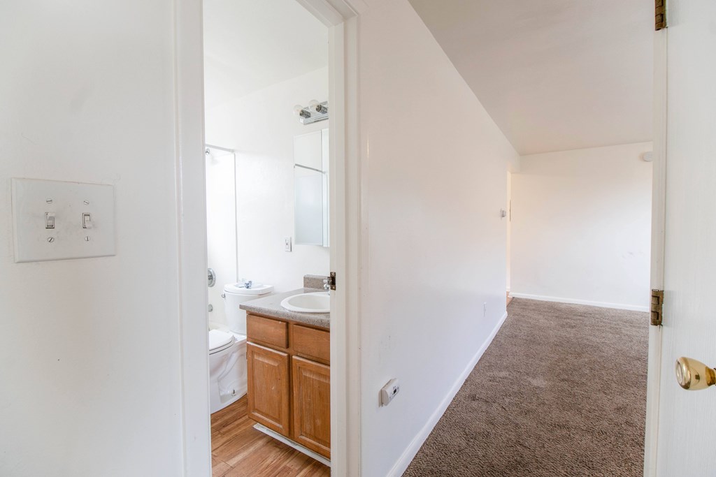 A white bathroom with a sink, toilet, and wooden cabinet.