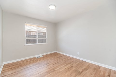 A room with wooden flooring and a window with blinds.
