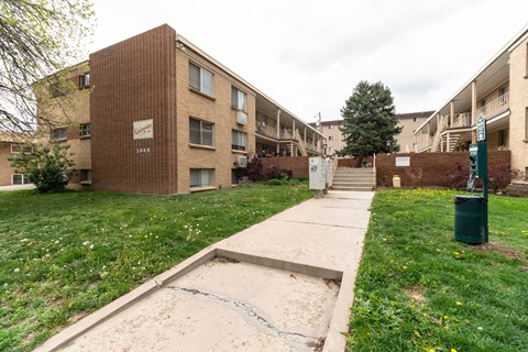 Apartment complex with a green trash can and a concrete pathway.