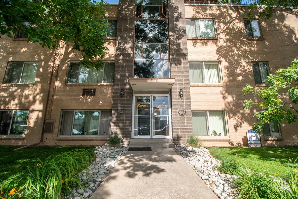 A building with a grey door and windows with white curtains.