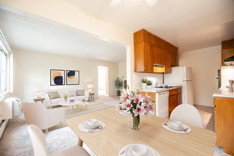 A dining room with a table set for two and a kitchen area in the background.