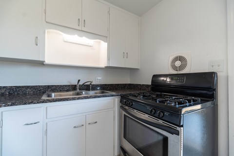 A black stove top oven sits on a granite countertop in a kitchen with white cabinets.