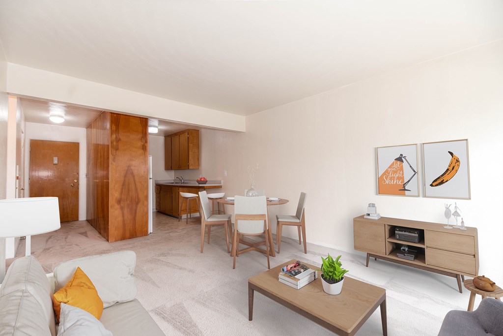 A living room with a grey couch, a coffee table, a dining table with chairs, a TV stand, and two framed pictures on the wall.