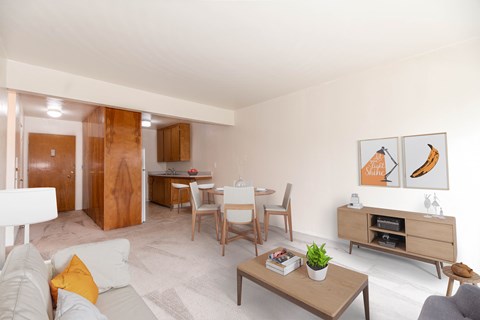 A living room with a grey couch, a coffee table, a dining table with chairs, a TV stand, and two framed pictures on the wall.