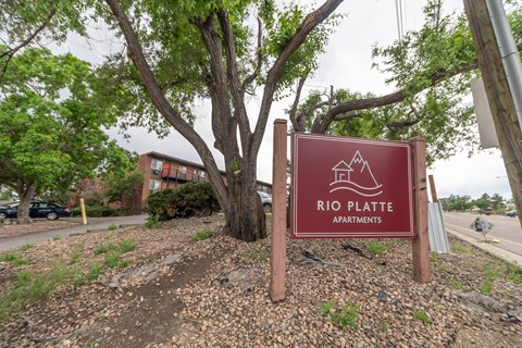 A sign for Rio Platte Apartments is displayed in front of a tree.