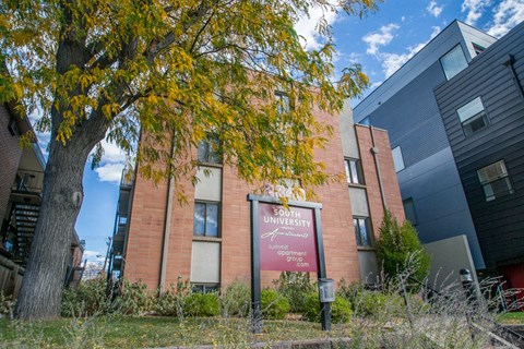 a brick building with a sign in front of a tree