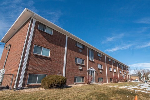 A red brick apartment building with a green bush in front.