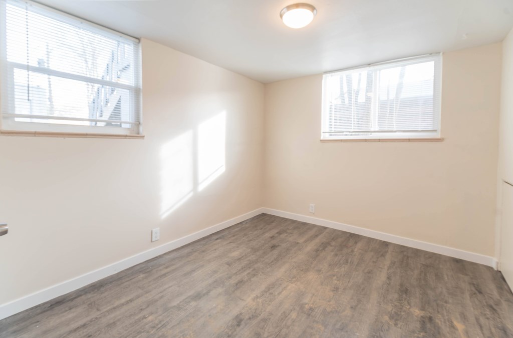 A room with wooden flooring and two windows.