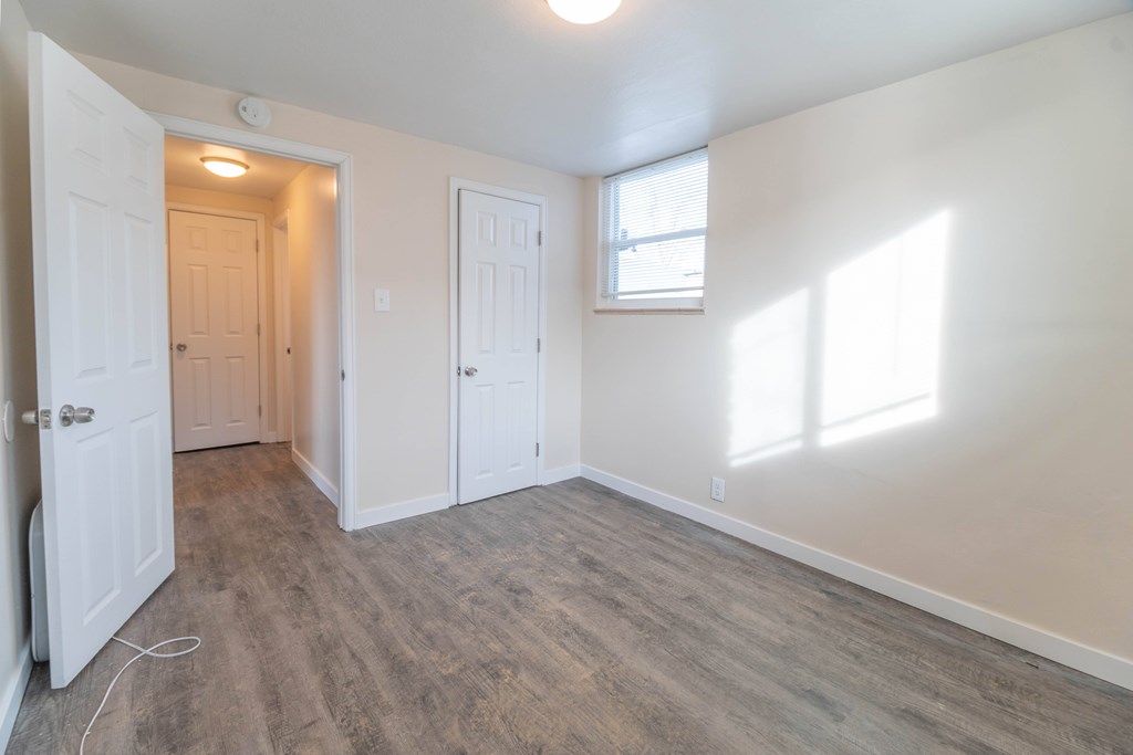 A room with white walls and wood flooring with a doorway leading to another room.