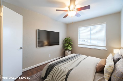 A bedroom with a bed, a ceiling fan, a television, and a window.