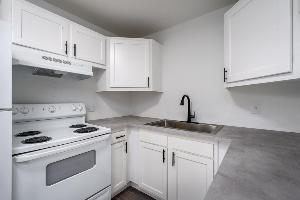 A white kitchen with a stove, sink, and cabinets.