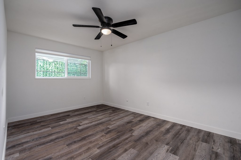 A room with a ceiling fan and a window with a view of trees.
