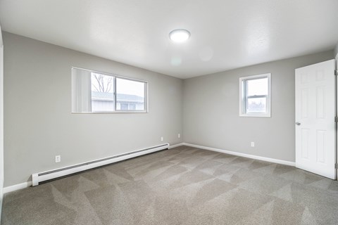 A room with a carpeted floor and two windows.