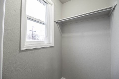 A white shelf is mounted on a white wall next to a window.