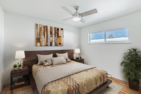 A bedroom with a bed, nightstand, and a plant.