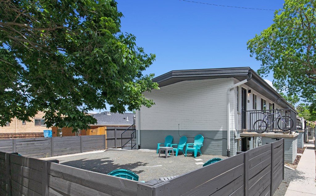 the back yard of a white house with blue chairs and a fence