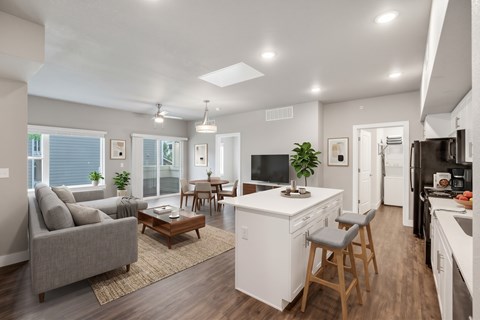 A well-lit, modern kitchen and living room with a grey sofa, wooden coffee table, and a white kitchen island.