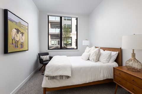 A bedroom with a bed, nightstand, chair, and a painting on the wall.