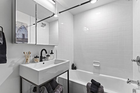 A white bathroom with a sink, mirror, and bathtub.