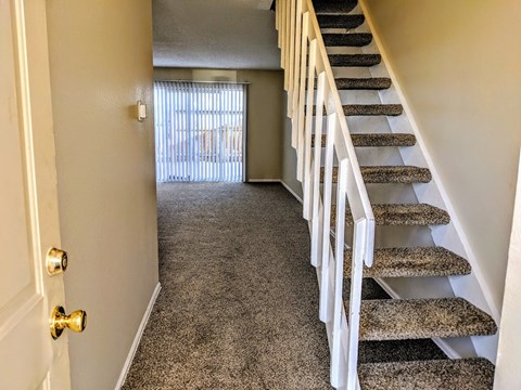 a carpeted hallway with stairs and a door to a living room